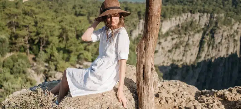 Woman in a hat sitting on a rock with mountains behind her, while thinking about NH Moving Trends 2022;