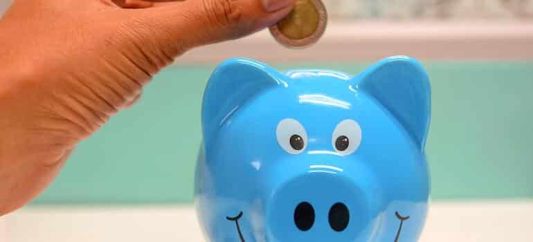 A person putting money inside a blue piggy bank for downsizing after relocation