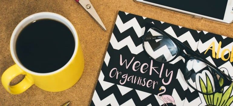 A weekly planner next to a cup of coffee