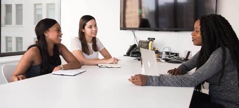 Three women sitting in an office and talking about office relocation checklist